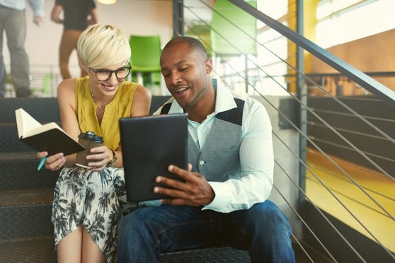 Two people sitting and looking at a tablet.